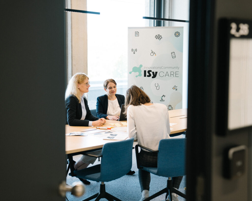 Arbeitsgruppe bei der Arbeit am Tisch mit dem ISyCARE Rollup im Hintergrund